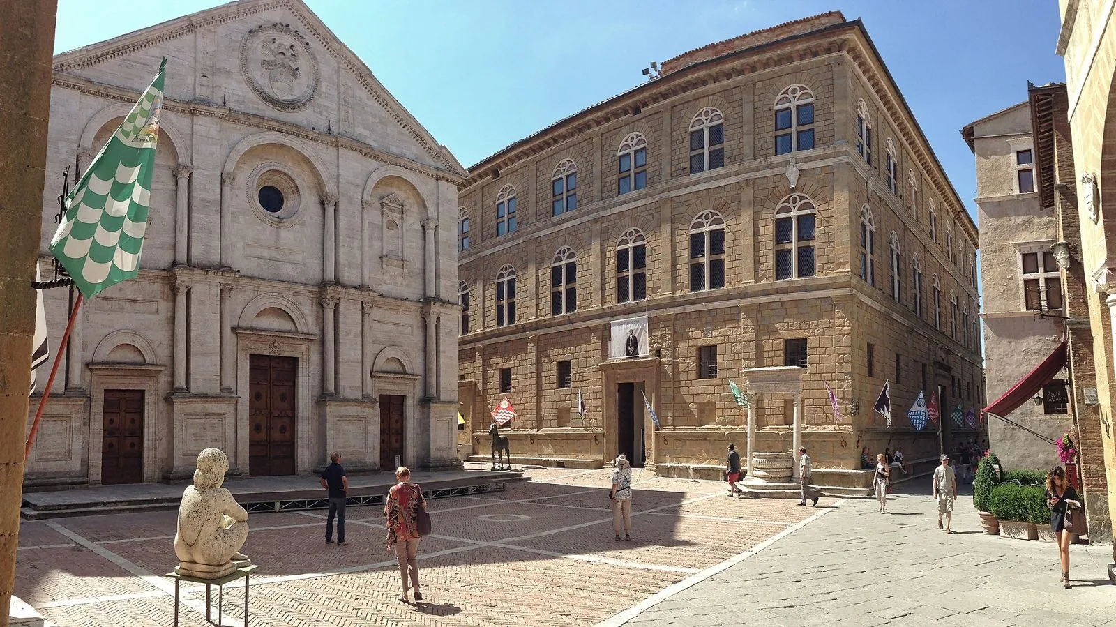 Piazza Pio II a Pienza con la Cattedrale, Palazzo Piccolomini, il pozzo e le bandiere dei rioni esposte